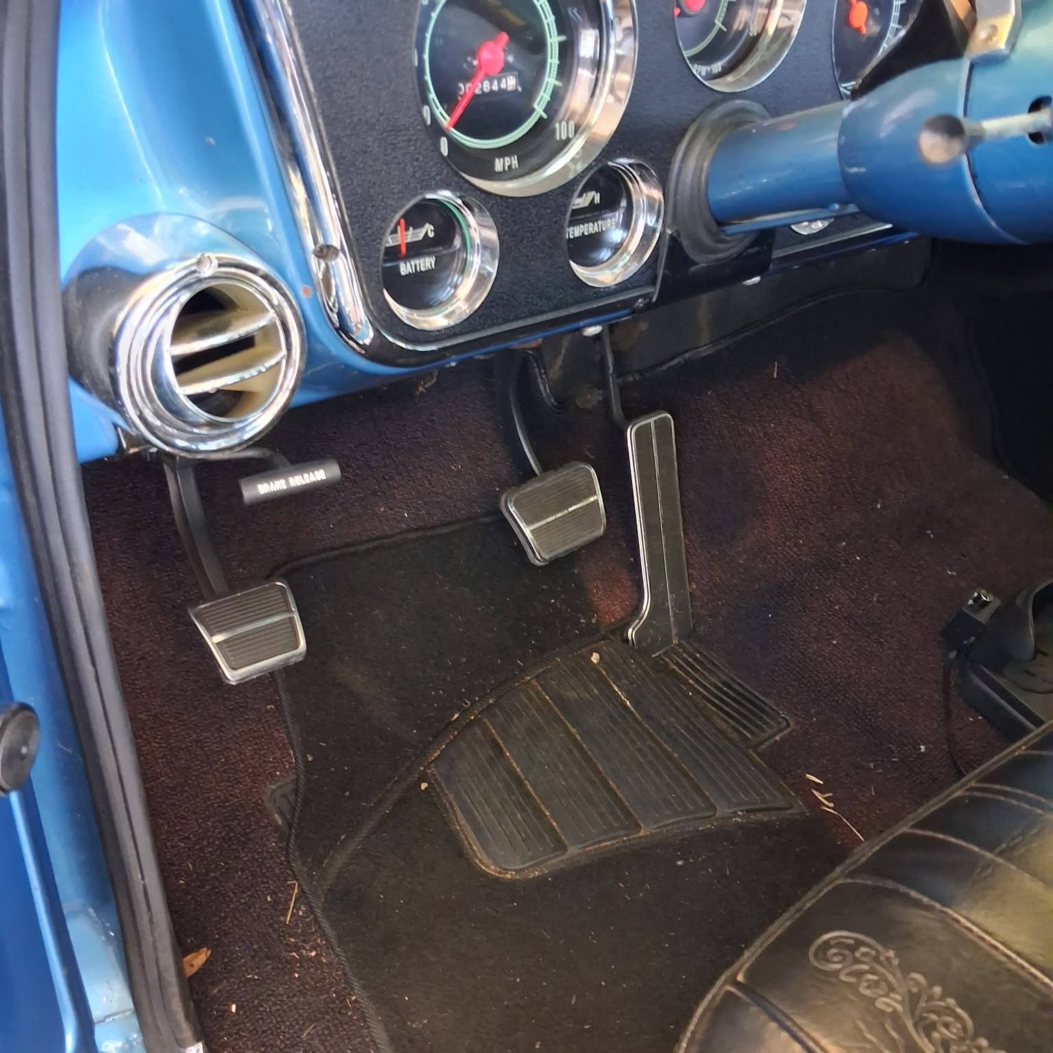 Classic truck dash, chrome gauges, and three pedals inside a vehicle in the shop.